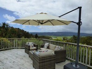 A deck with wicker furniture, a table, and a large umbrella.