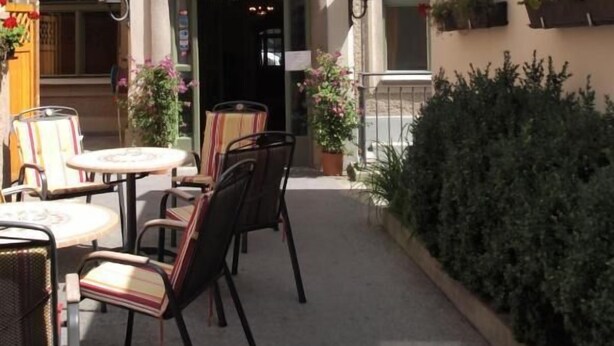 Un patio con mobiliario exterior, entrada de un edificio y plantas en macetas.