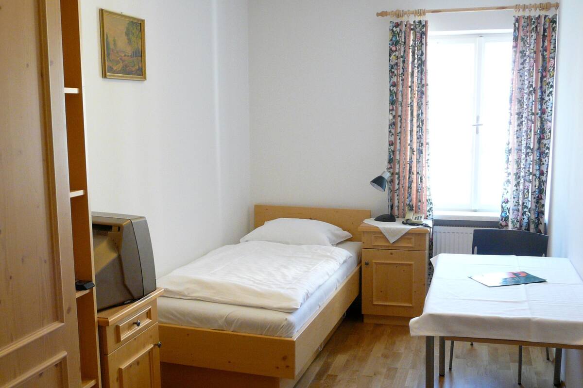 A small, clean room with a bed, a nightstand, a desk, and a radiator.