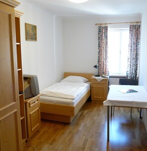 A small, clean room with a bed, a nightstand, a desk, and a radiator.