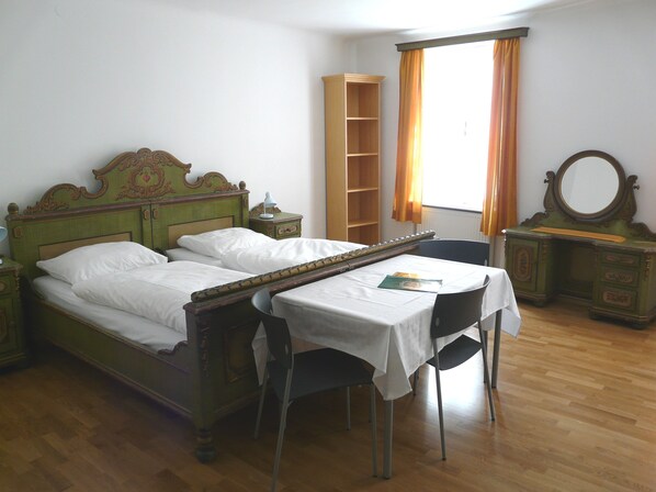 A room with a bed, a table, a chair, a mirror, and a shelf.