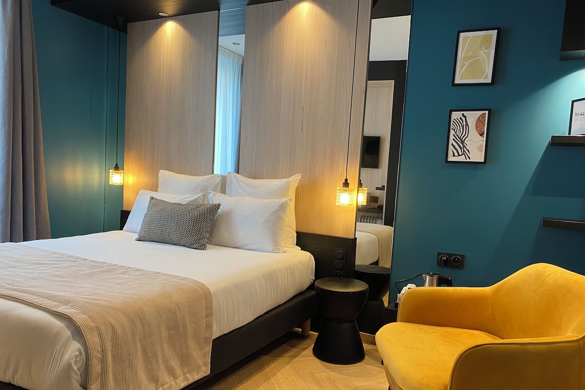 Una habitación de hotel moderna con una cama grande, mesitas de noche, una pequeña mesa redonda y un sillón amarillo.