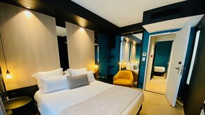 A modern hotel room with a large bed, bedside tables, a chair, and a bathroom visible through an open door. - Grand Hotel Clichy (Clichy)