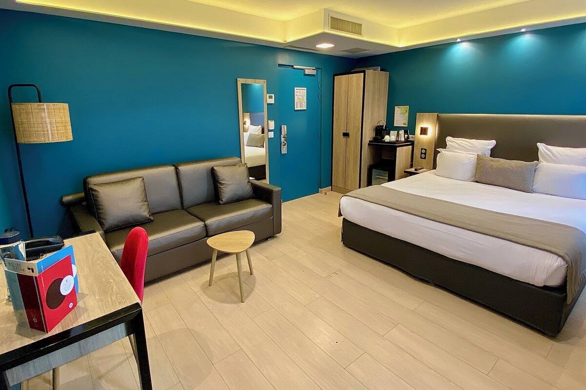 A hotel room with a bed, a sofa, a small table, a chair, and a desk.