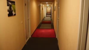 A hotel hallway with a red carpet, beige walls, and doors on both sides. - Hotel Quick Palace - Bourg Les Valence (Bourg-les-Valence)