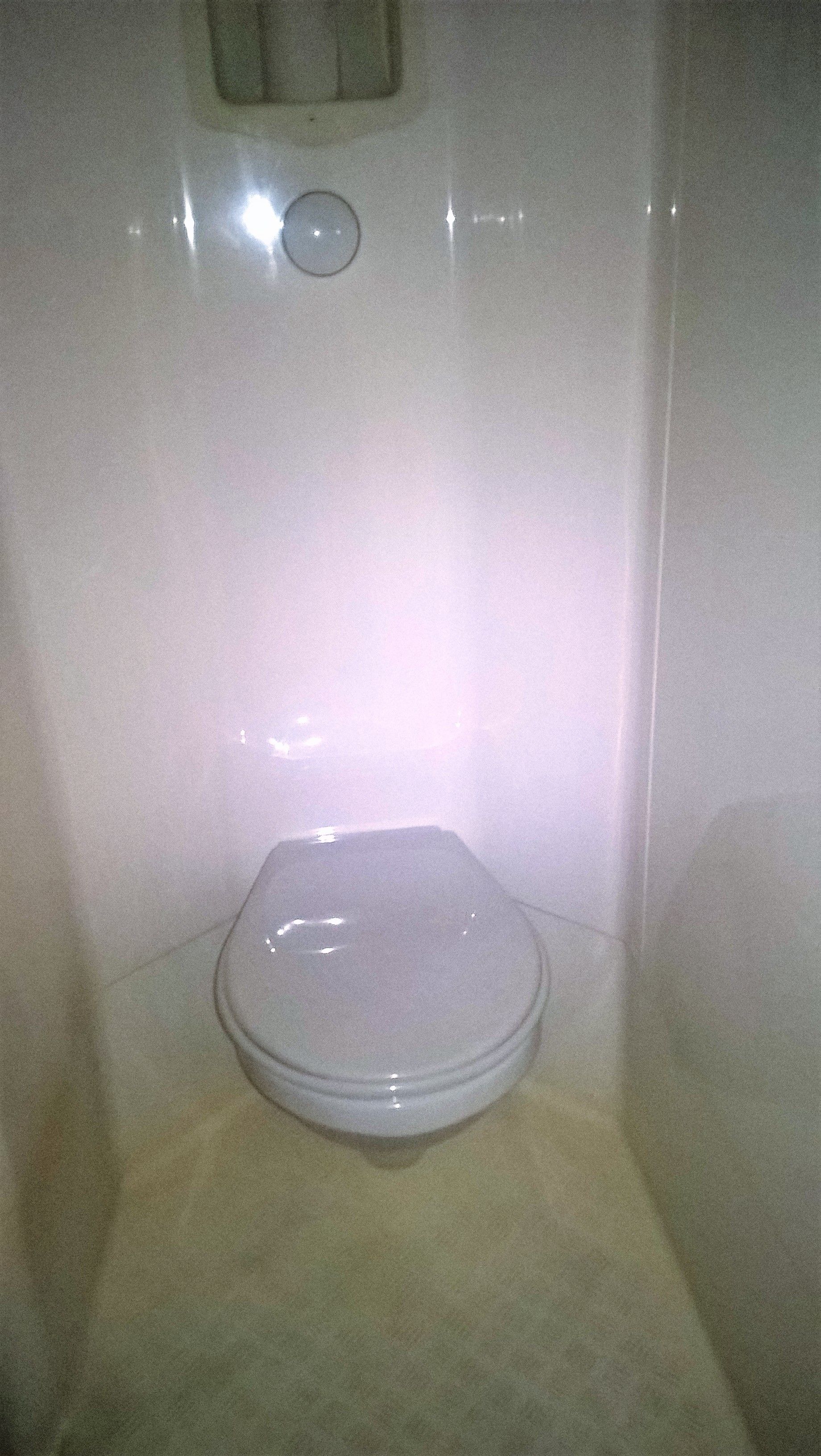 Een wit toilet in een badkamer met een effen muur en een klein raam erboven.