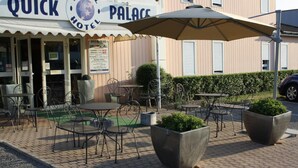 An outdoor seating area with tables and chairs, a large umbrella, and a sign for the Quick Hotel Palace. - Hotel Quick Palace - Bourg Les Valence (Bourg-les-Valence)