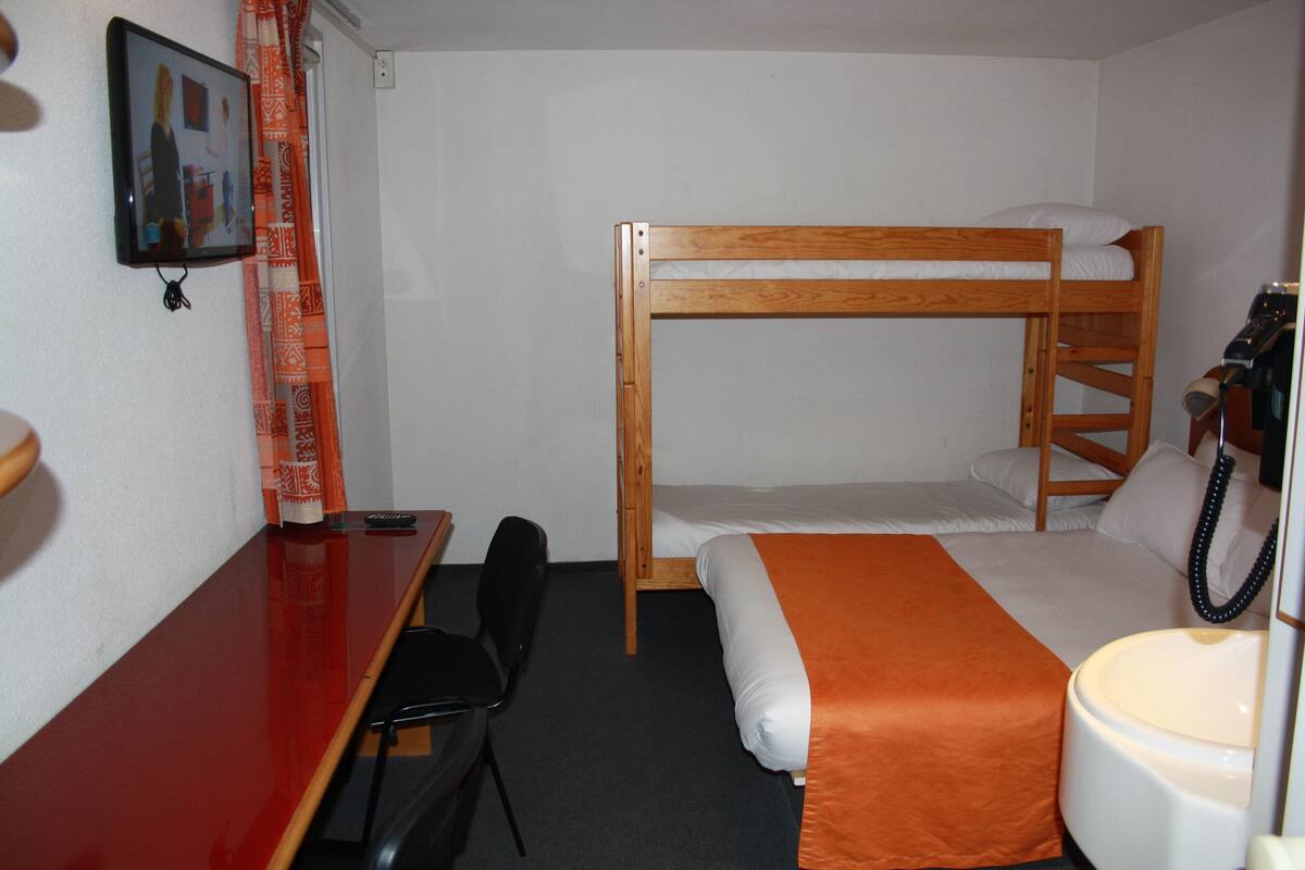 A bunk bed room with a desk, chair, and a small bathroom.