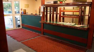 A reception area with a green counter, a wooden display case with menus, and a red carpeted entrance.
