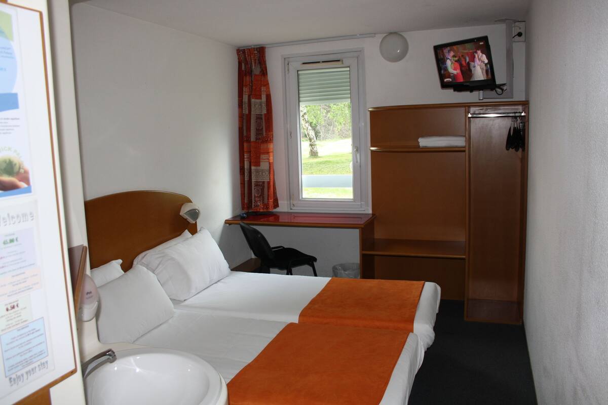 A hotel room with a bed, a desk, a chair, a TV, and a wardrobe.