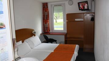 Habitación de hotel con una cama, un escritorio, una silla, un televisor y un armario.