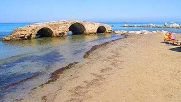 A stone bridge over calm waters, a sandy beach, and a clear blue sky. - Dimitra Hotel Apartments (Hersonissos)