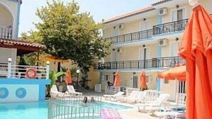 A swimming pool with lounge chairs and umbrellas, surrounded by a building with balconies. - Dimitra Hotel Apartments (Hersonissos)