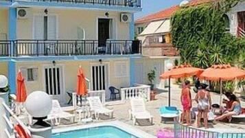 A pool area with lounge chairs and umbrellas, a building with balconies, and a clear blue sky.