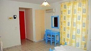 A room with a bed, a desk, and a chair. There is a door leading to another room and a window with curtains. - Dimitra Hotel Apartments (Hersonissos)