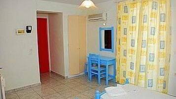 A room with a bed, a desk, and a chair. There is a door leading to another room and a window with curtains.