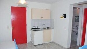 A compact kitchen with a red door, a small refrigerator, and a white countertop. - Dimitra Hotel Apartments (Hersonissos)