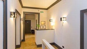 Een hotelgang met een receptiebalie, ingelijste foto's en wandlampen.