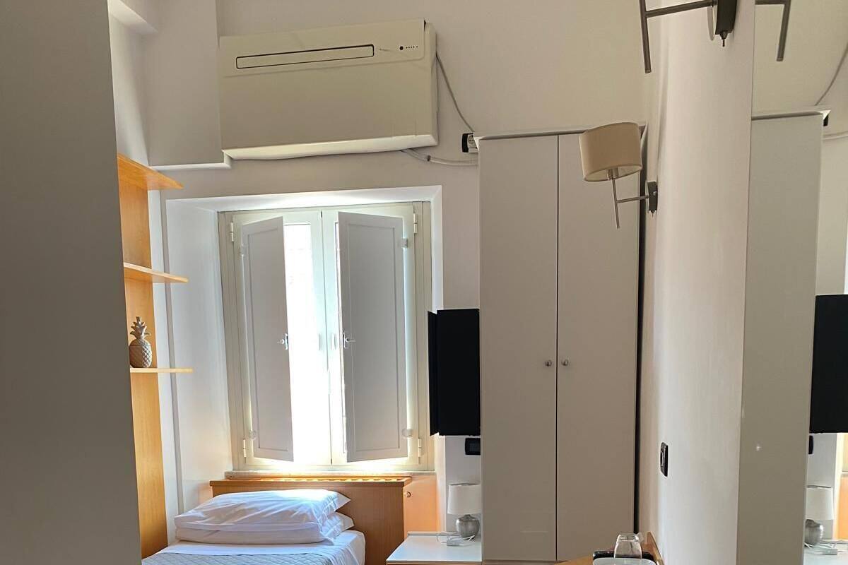 Habitació compacta amb un llit, taules de nit, escriptori i un armari.