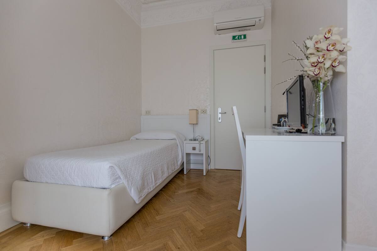 Habitació d'hotel amb llit, taulella de nit i escriptori amb un ram de flors.