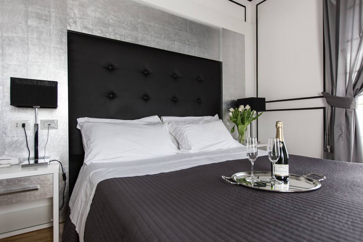 Habitació d'hotel moderna amb un llit gran, una taula de nit amb una làmpada i un servei amb xampany i copes.