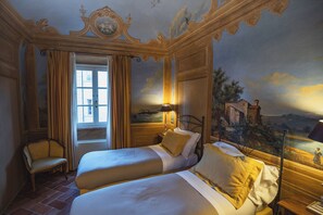 A room with two beds, a chair, and a mural on the wall. - Borgo Di Colleoli Resort (Palaia)