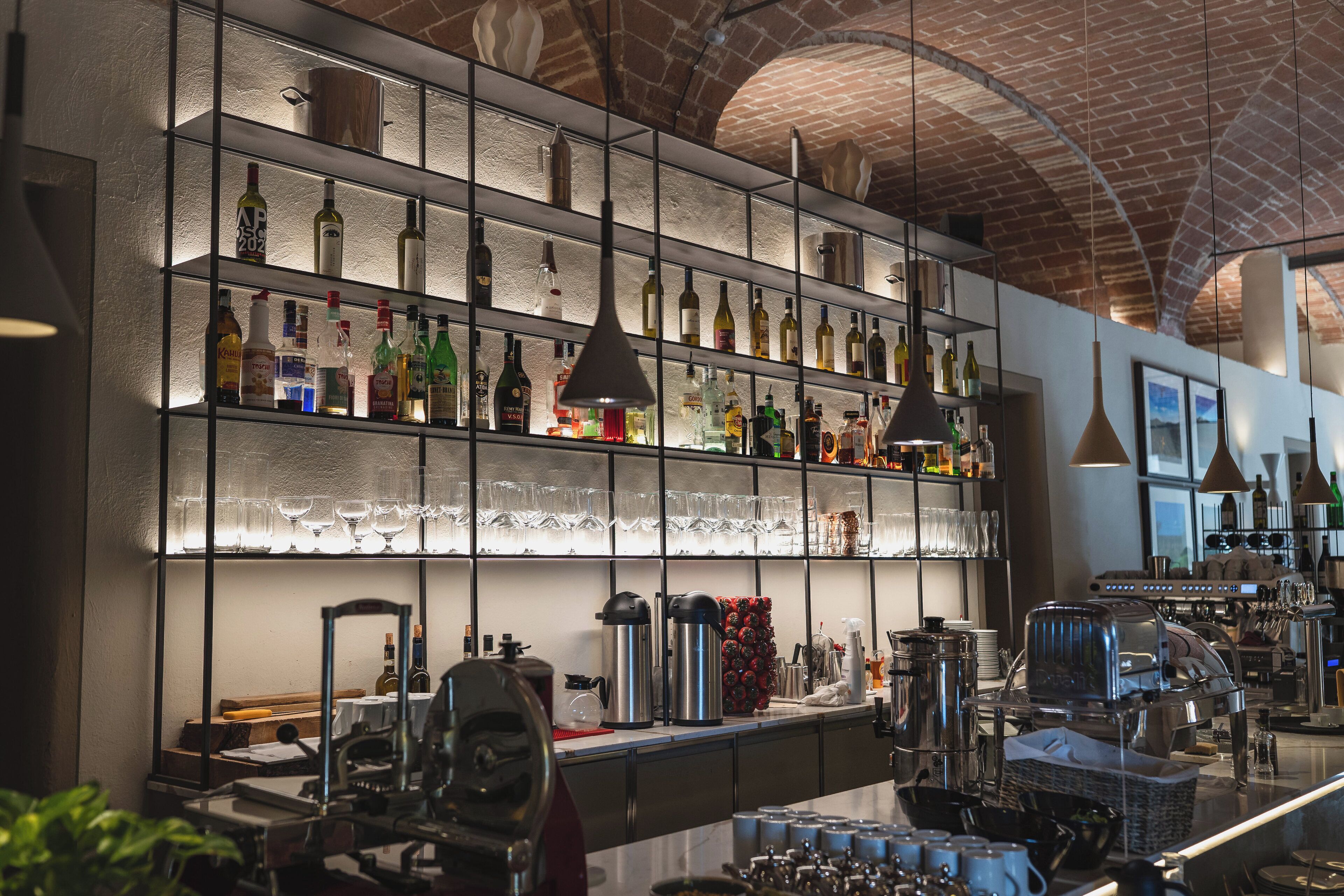 A bar area with shelves of bottles and glasses, a coffee machine, and a counter with various items.