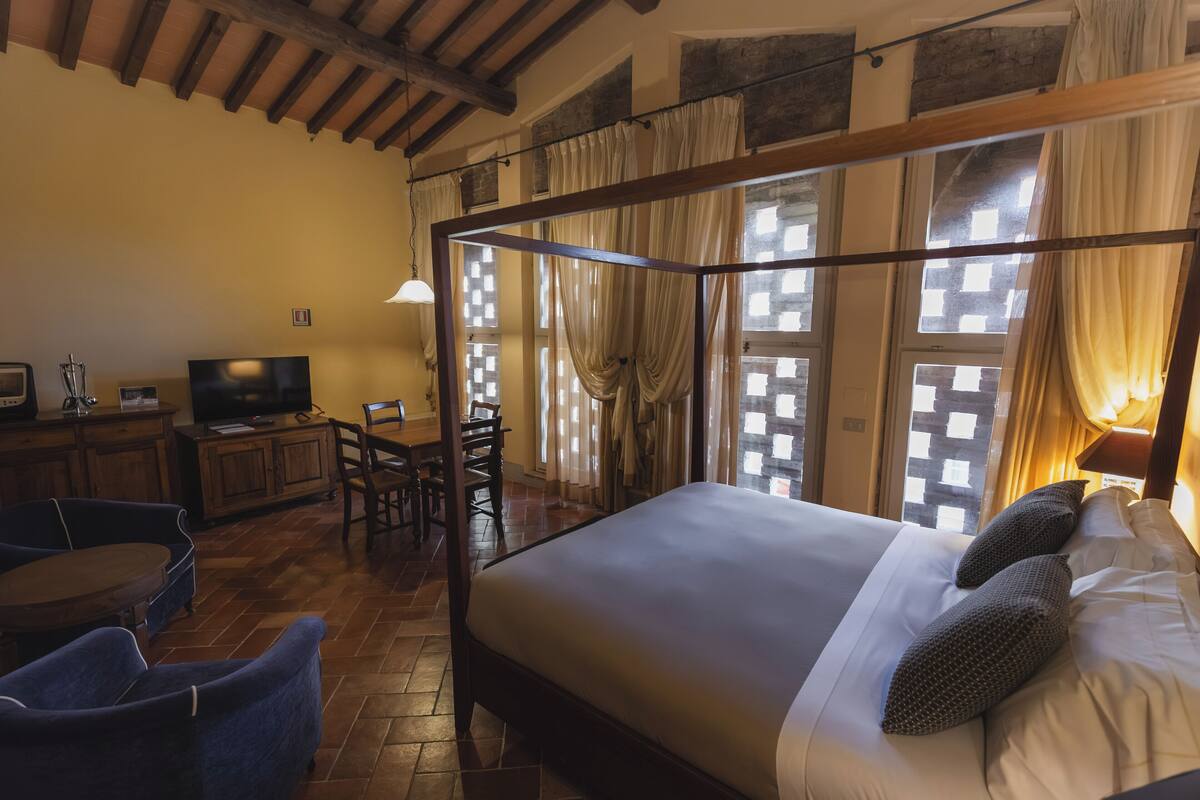 Un dormitorio con cama con dosel, un escritorio con televisor y una zona de comedor con sillas y una mesa.