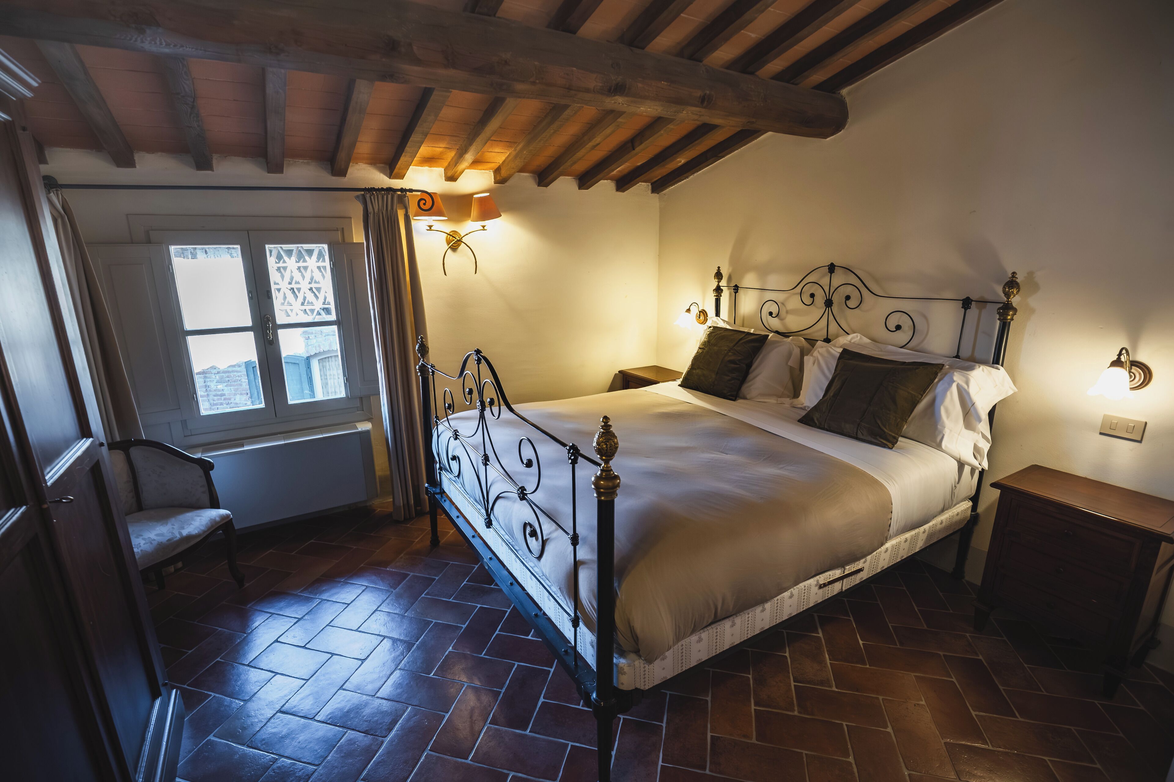 A bedroom with a large bed, a chair, a nightstand, and a window with curtains.