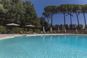 A clear swimming pool with lounge chairs and umbrellas, surrounded by trees. - Borgo Di Colleoli Resort (Palaia)
