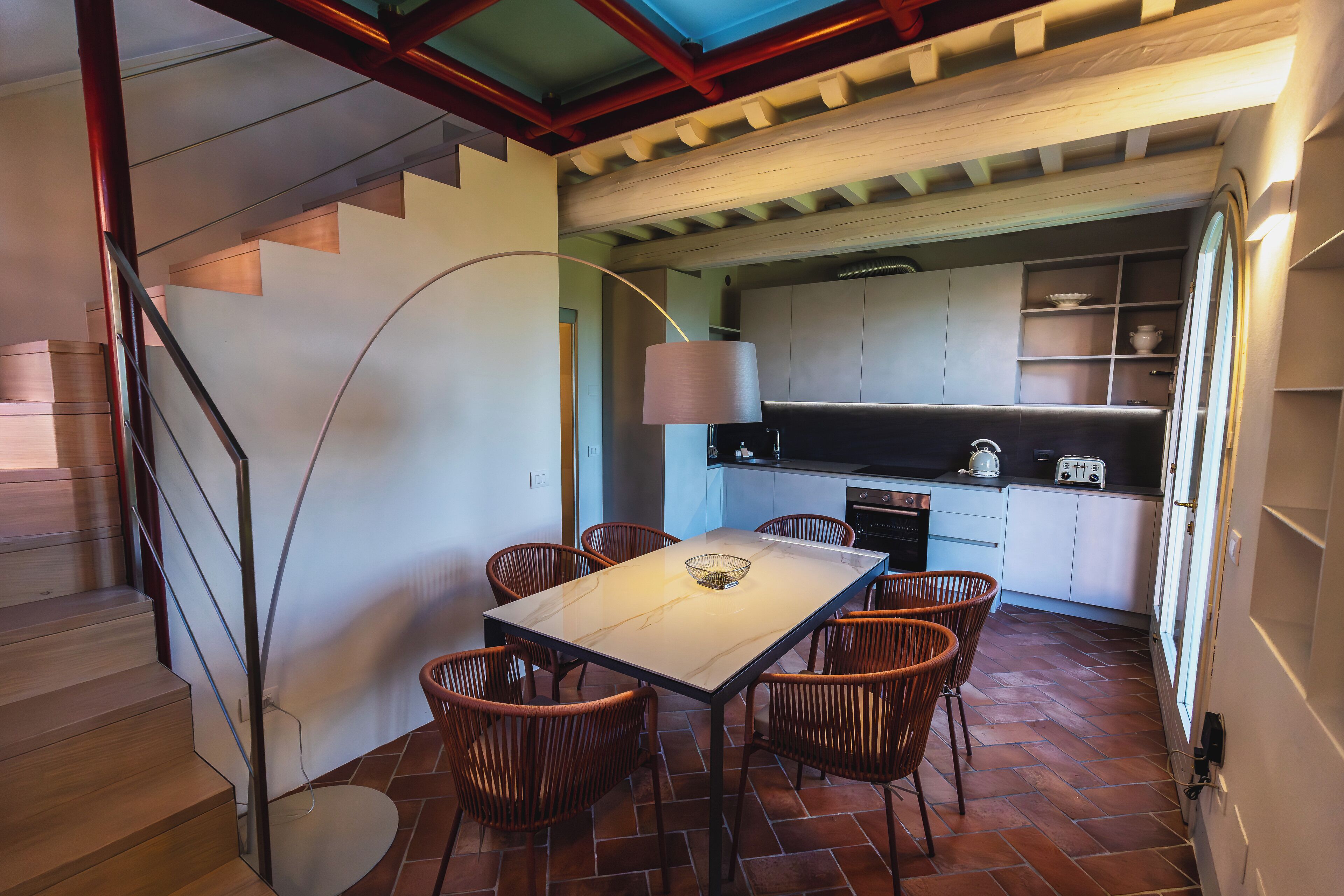 A dining area with a table and chairs, a kitchen in the background, and a staircase leading to another level.