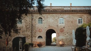 A stone building with an arched entrance, outdoor seating, and a gravel courtyard. - Borgo Di Colleoli Resort (Palaia)