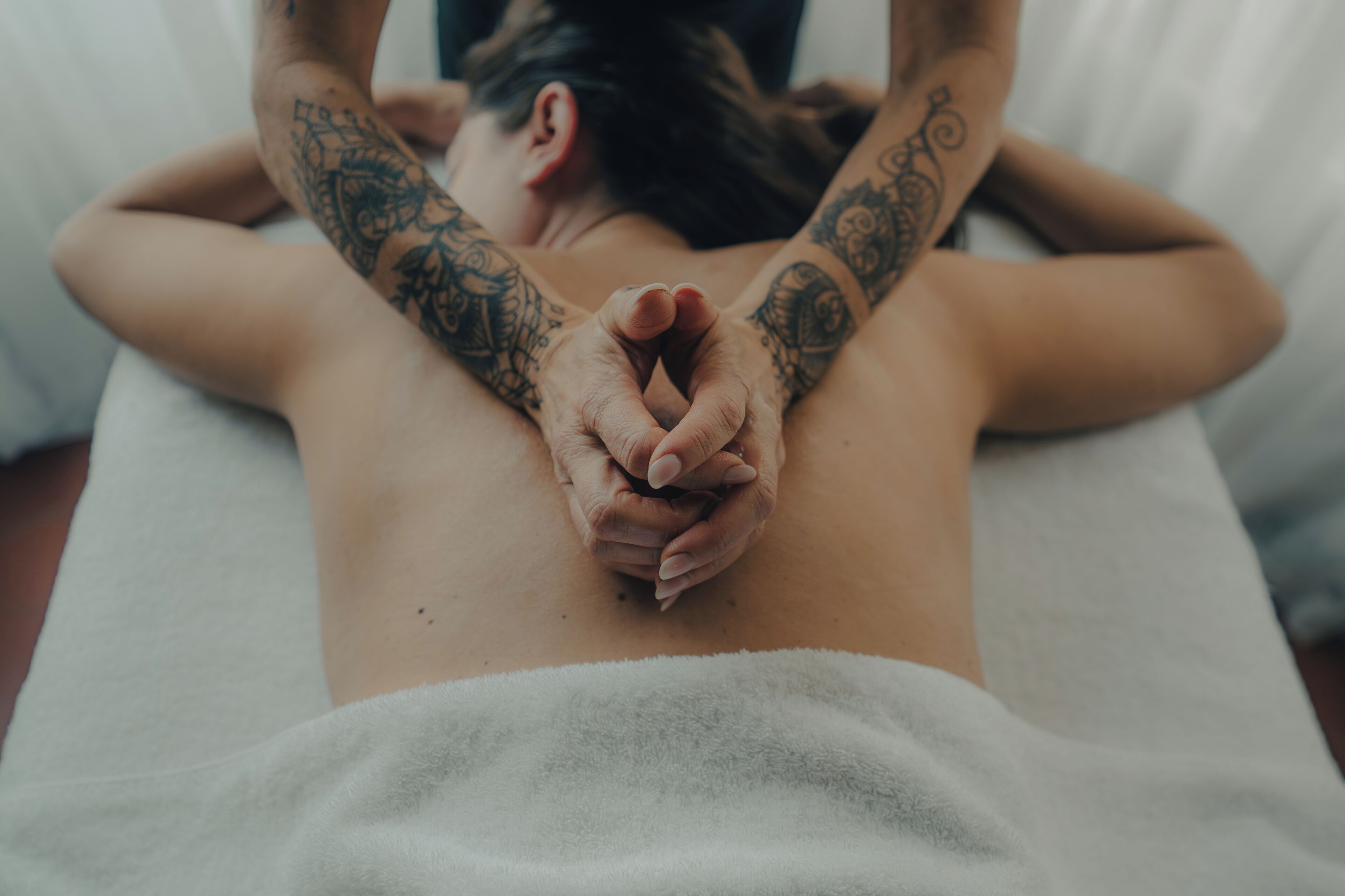 En person får en massage på ryggen och har tatueringar på armarna.