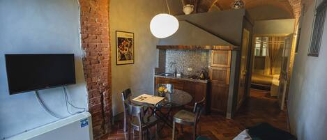 Un salon confortable avec un téléviseur, une table à manger avec des chaises, une cuisine avec un plan de travail et un escalier menant à un autre niveau.