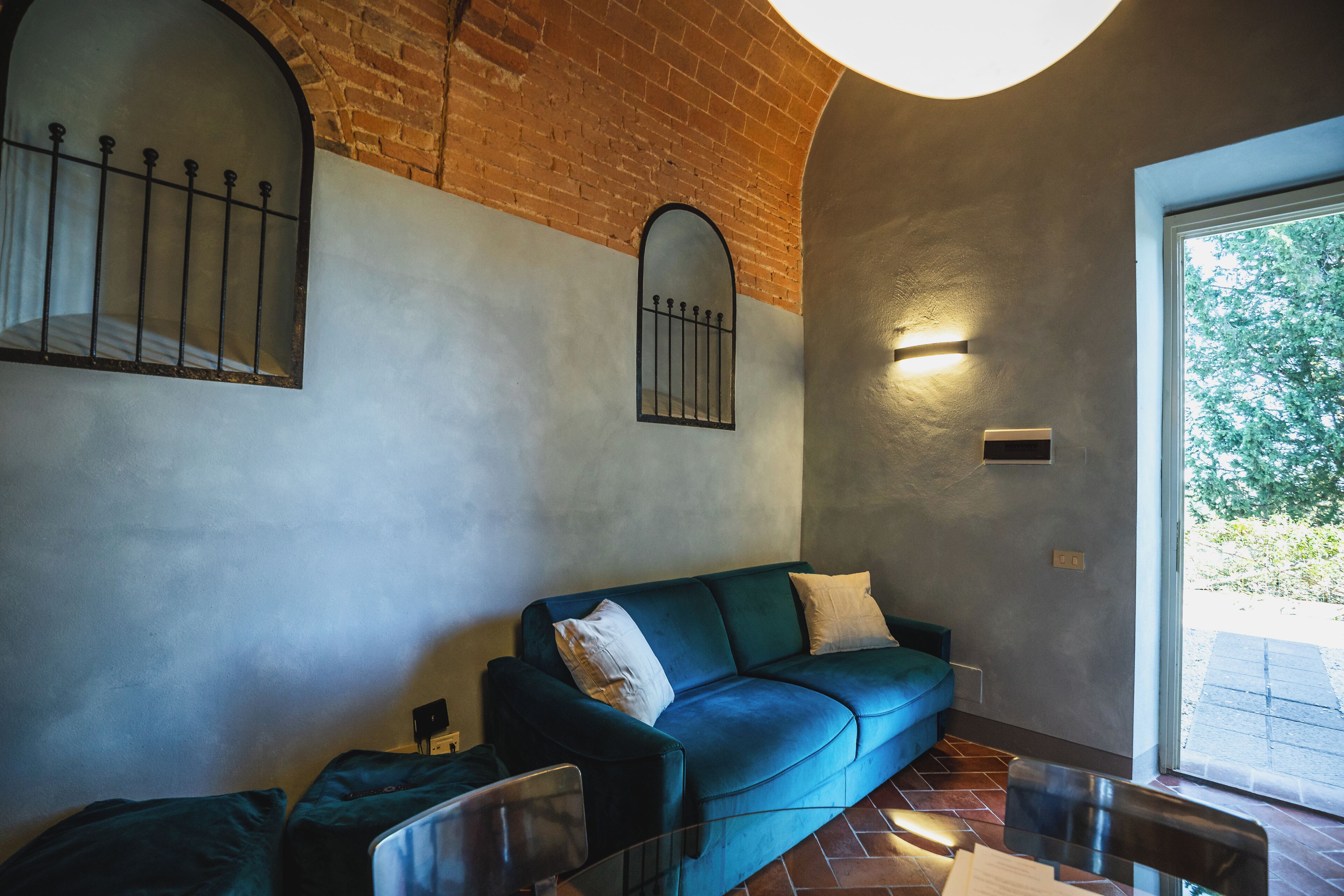 A living room with a blue sofa, a glass coffee table, and a brick wall with arched windows.