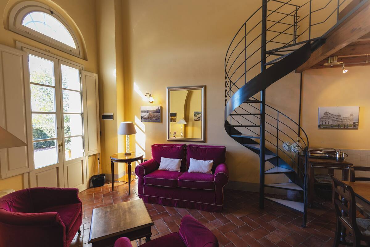 Un salón espacioso con un ventanal grande, un sofá púrpura, una mesa de centro de madera y una escalera de caracol.