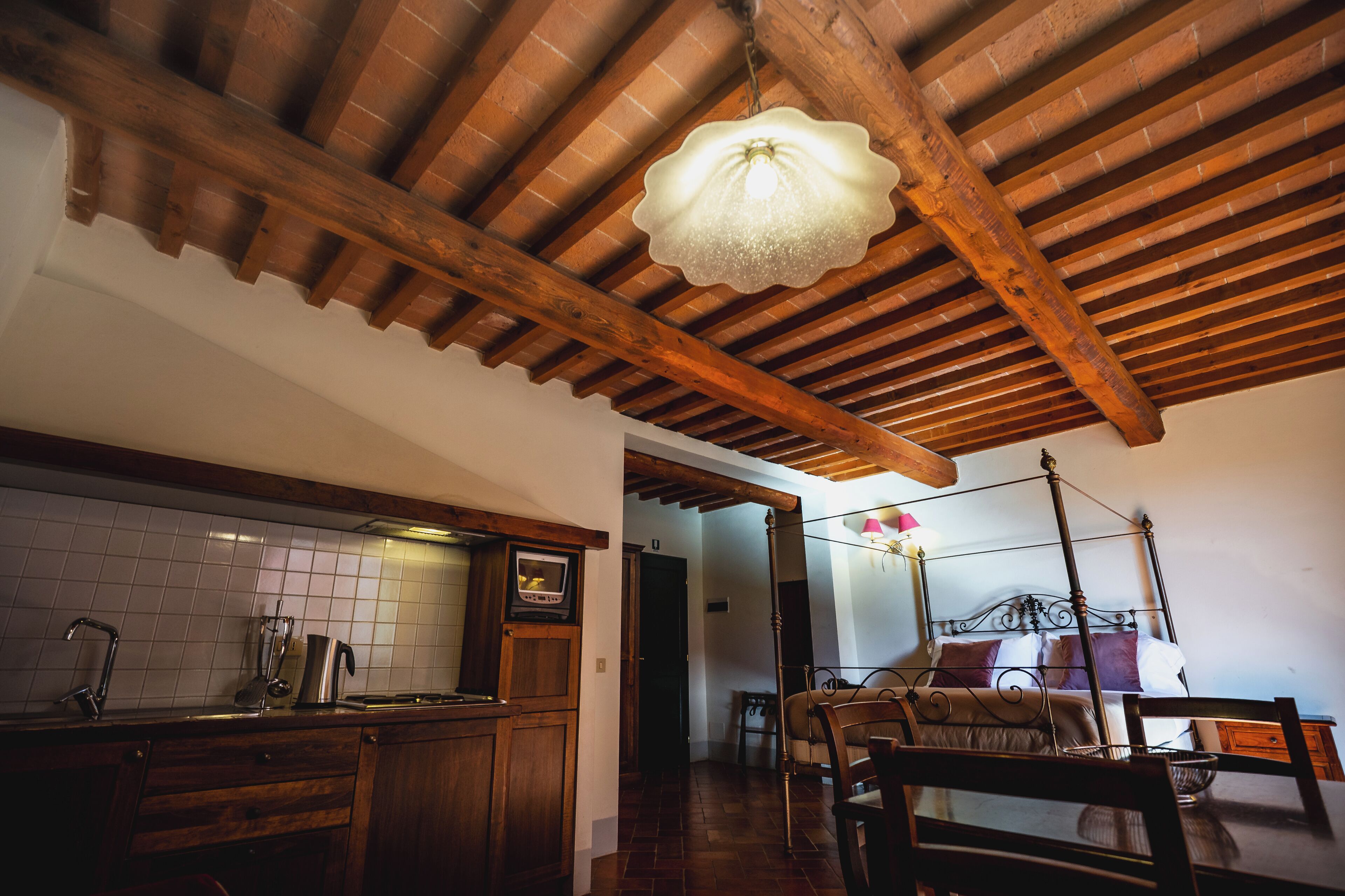 Cucina rustica con travi in legno, lampadario a sospensione e piastrelle a parete.