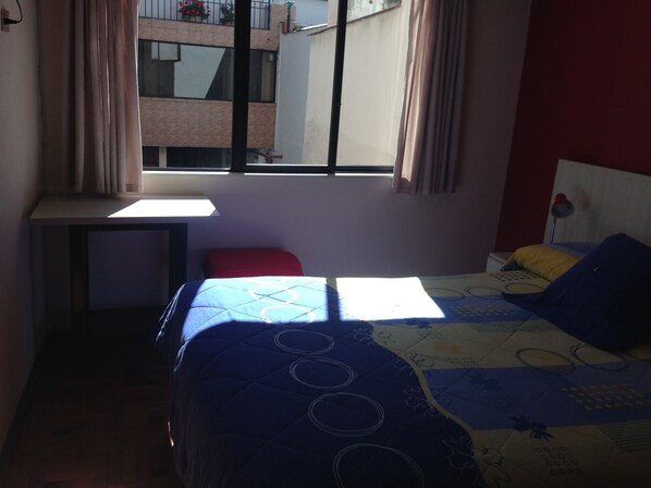 A bedroom with a bed, a desk, and a window.