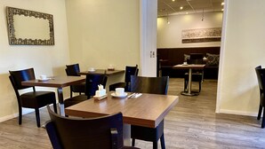 Ein Hotel-Speisebereich mit Holztischen und schwarzen Stühlen, einem gerahmten Kunstwerk an der Wand und Blick ins Restaurant.