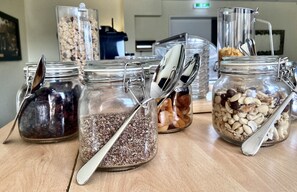 Une table sur laquelle se trouvent plusieurs bocaux en verre contenant différents types d’aliments, chacun accompagné d’une cuillère.