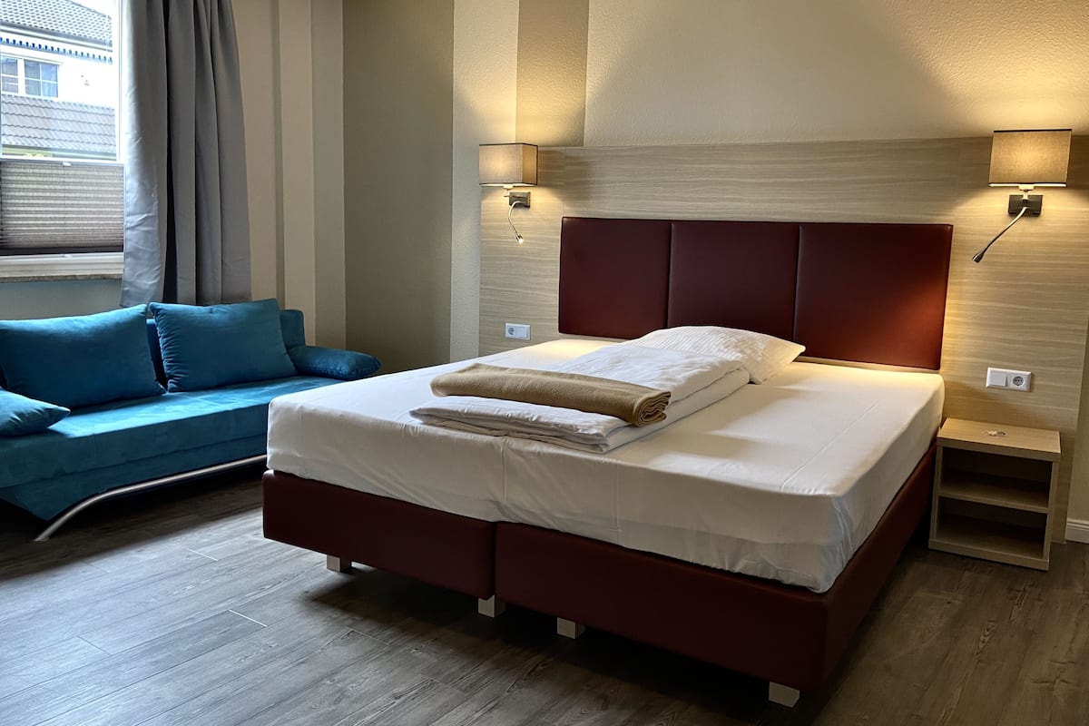 Una habitación de hotel moderna con una cama grande, un sofá y dos lámparas fijadas a la pared.