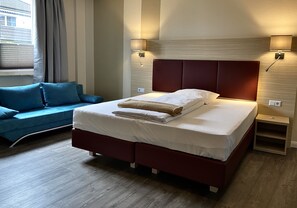 Une chambre d’hôtel moderne, dotée d’un grand lit, d’un canapé et de deux lampes fixées au mur.