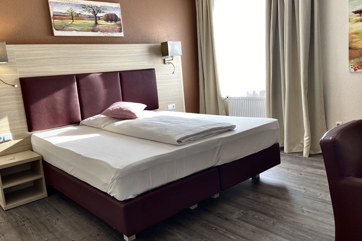 Una habitación de hotel con una cama grande, una mesita de noche, una lámpara y un cuadro en la pared.