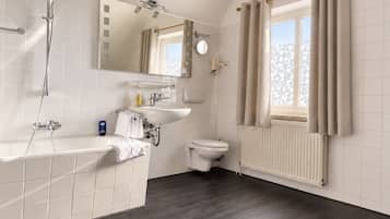 Ein modernes Badezimmer mit Badewanne, Toilette, Waschbecken und einem Fenster mit Vorhängen.