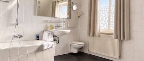 A modern bathroom with a bathtub, a toilet, a sink, and a window with curtains.