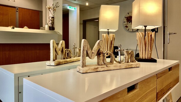 Ein Hotel-Rezeptionsbereich mit einer weißen Theke, Holoszillen und einer dekorativen Buchstaben 'M' in Form eines Ankers.
