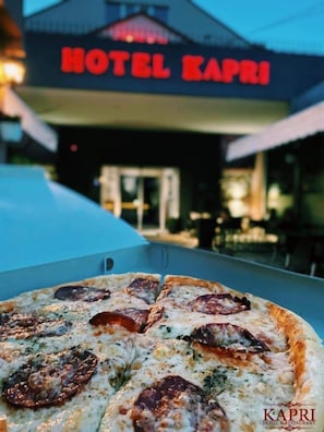 A pizza in a box with a view of Hotel Kapri in the background. - Hotel Kapri (Bitola)
