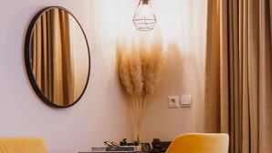 Una habitación moderna con un sofá amarillo, un espejo redondo, un escritorio con una computadora y una lámpara colgante.
