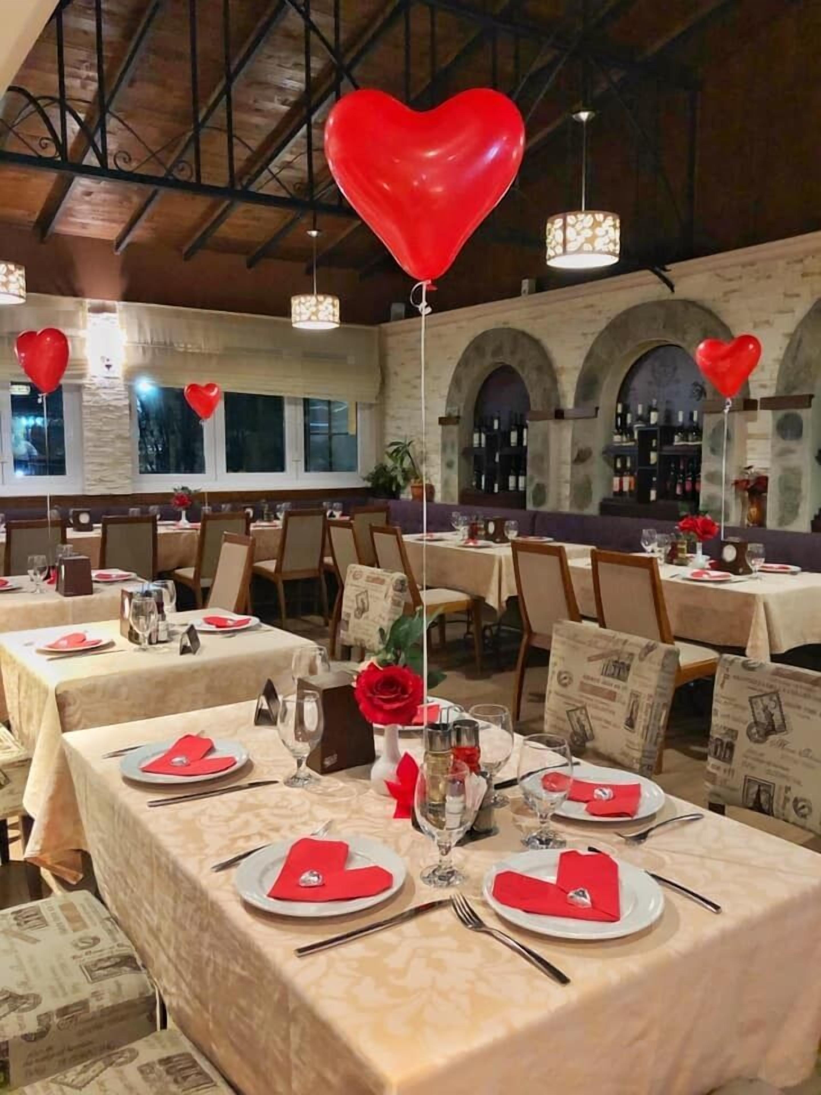 A restaurant with tables set for dining, featuring heart-shaped napkins and red balloons.