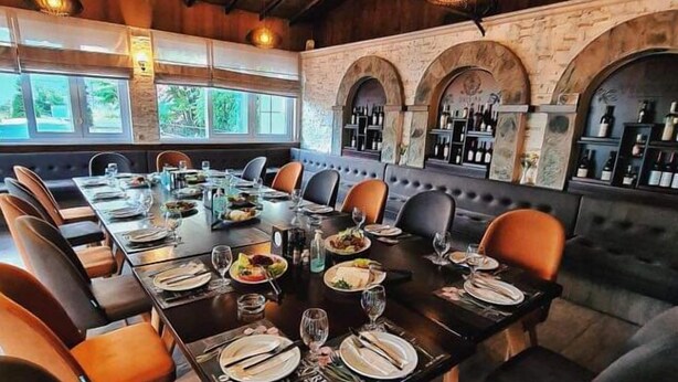 Un restaurante con una larga mesa común, asientos acolchados y una zona de bar con estanterías llenas de botellas.